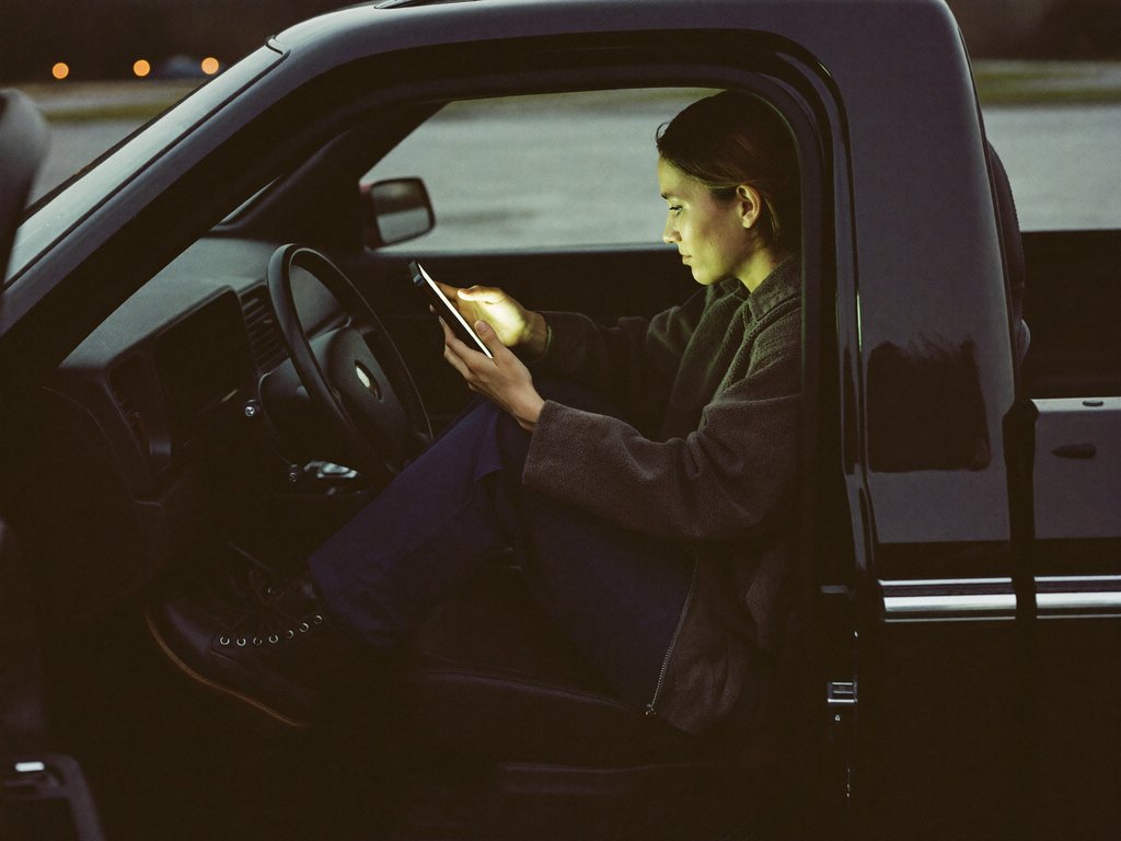 A tradesperson sitting in the open door of her parked truck at dusk, about to tap the one button on a landing page